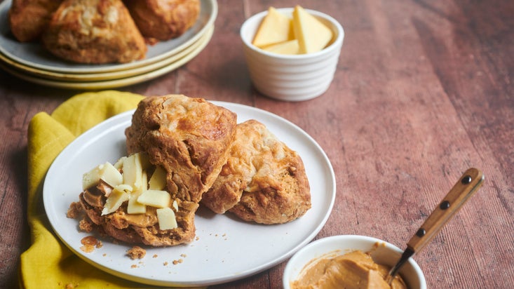 Scone on a plate, one with a spread and small pieces of cheese on top